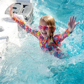 A smiling child with their hands in the air while floating in a swim spa.